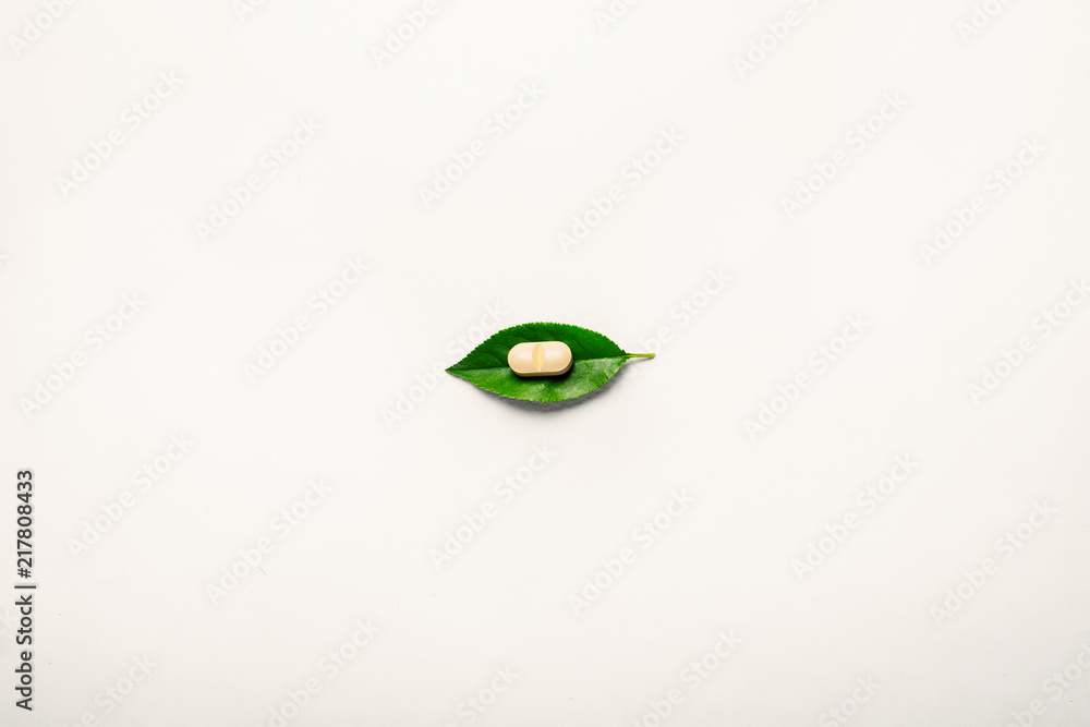One vegetable supplement tablet on a green leaf. Light background, minimalism. The concept of alternative medicine