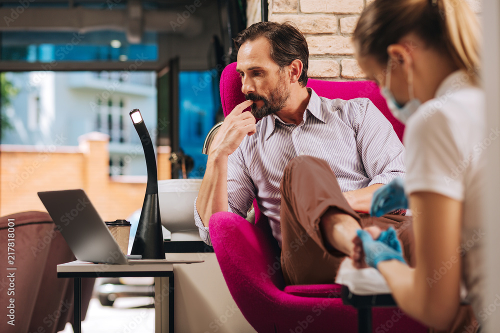 Luxurious nail bar. Musing mature man getting toenails done and staring at screen Luxurious nail bar. Musing mature man getting toenails done and staring at screen