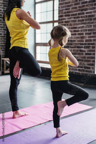 Mother and daughter practicing yoga together meditating standing on one leg with hands in prayer