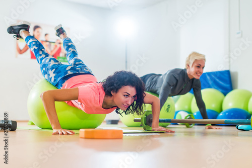 Two women exercising with stability balls doing push-ups in a gym class