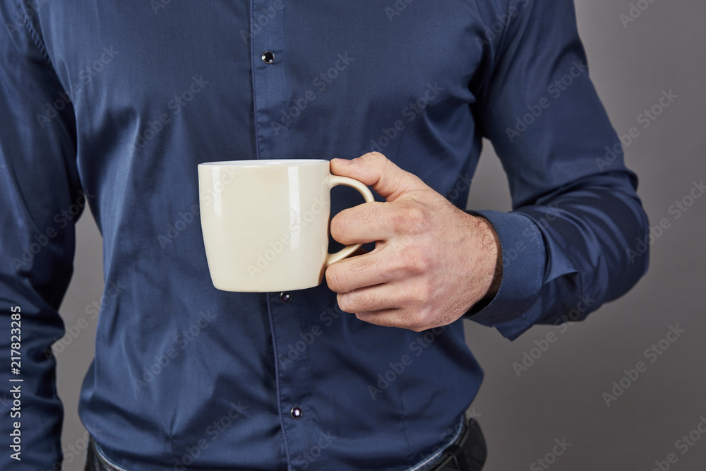 Handsome bearded man with stylish hair beard and mustache on serious face in shirt holding white cup or mug drinking tea or coffee in studio on grey background Handsome bearded man with stylish hair beard and mustache on serious face in shirt holding white cup or mug drinking tea or coffee in studio on grey background