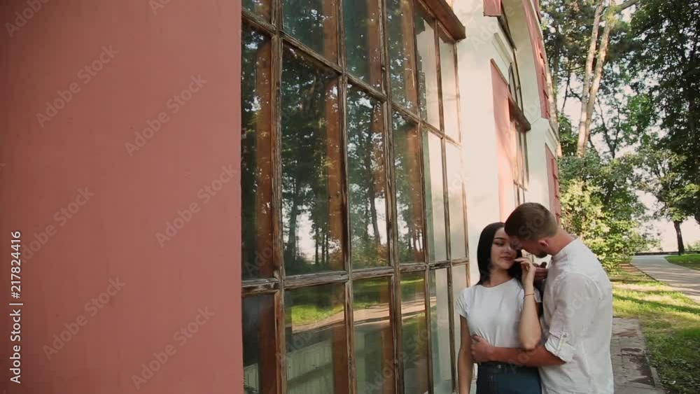 A loving couple hugs and kisses near a building with large windows in the park. A loving couple hugs and kisses near a building with large windows in the park.