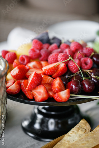 Fresh Fruit platter on banquet table at business or wedding event venue. Self service or all you can eat - raspberry, strawberry, cherry, Fig, apricote. Table with cold snacks and tableware