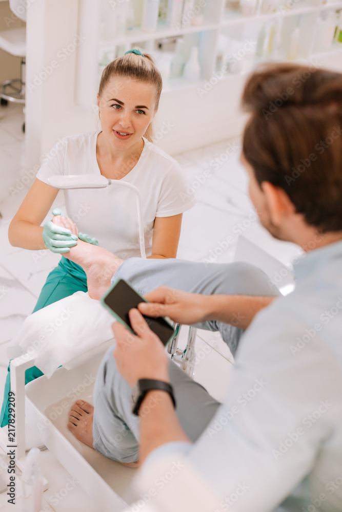 Obraz premium Massage therapist. Blonde-haired appealing massage therapist feeling cheerful while talking to her constant client