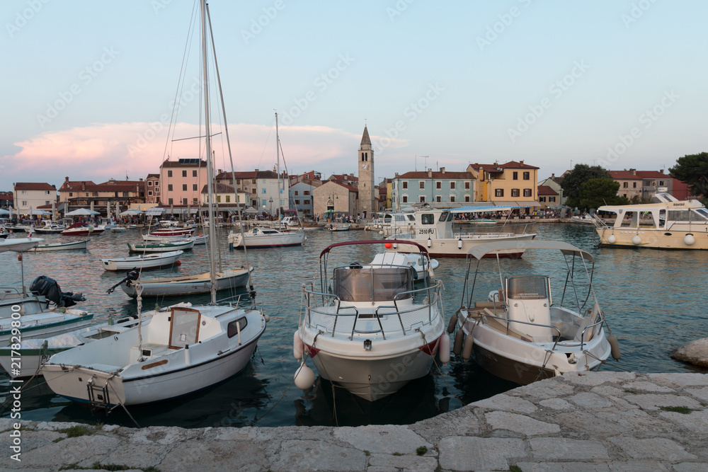 Obraz premium Fazana, Croatia - July 28, 2018: View of the harbour of Fazana with the market and the church in the background in the evening sun, Croatia.