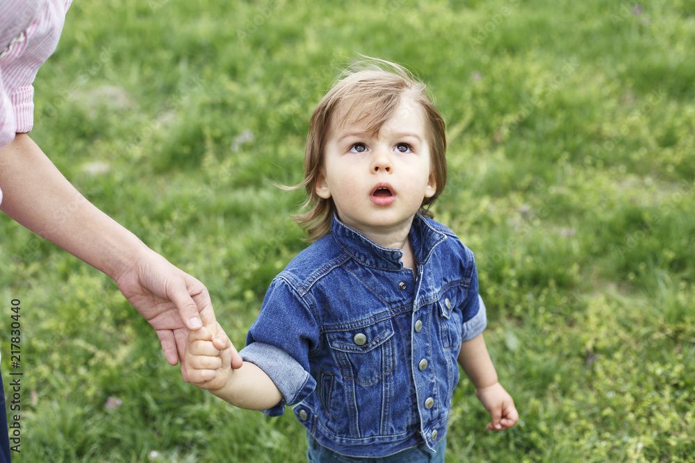 Family scene , closeup parent and baby holding hand together. Cute toddler boy with wondering face, looking up, holding mum's finger Family scene , closeup parent and baby holding hand together. Cute toddler boy with wondering face, looking up, holding mum's finger