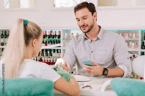 Caring about look. Bearded dark-haired metrosexual caring about his look getting manicure in salon photo