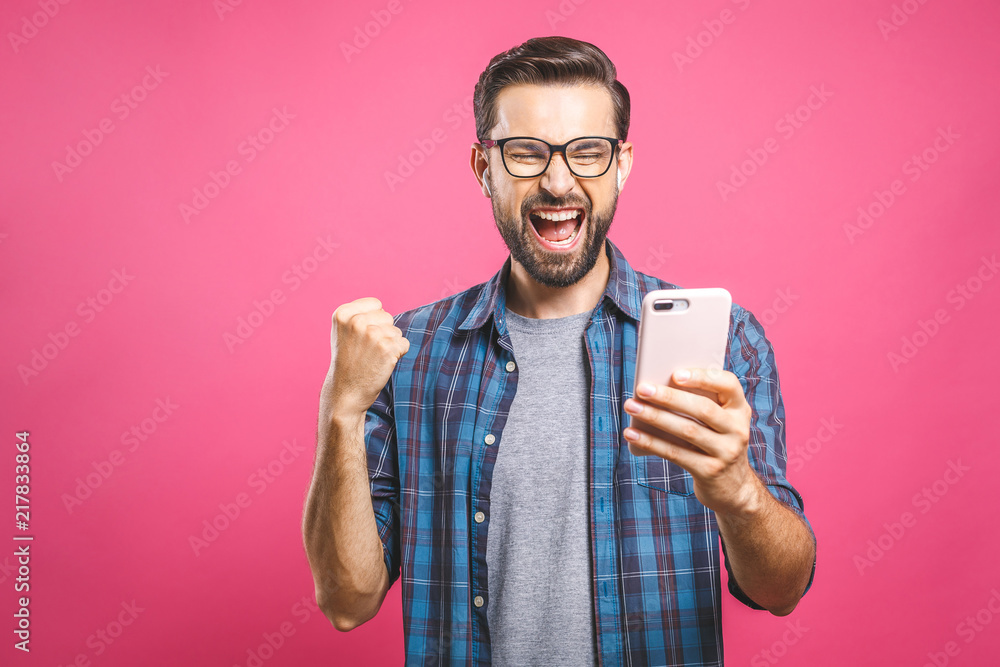 I'm a winner! Happy man holding smartphone and celebrating his success over pink background.