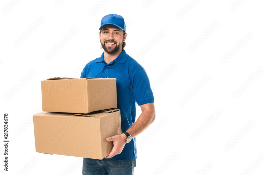 handsome happy young delivery man holding cardboard boxes and smiling at camera isolated on white - obrazy, fototapety, plakaty 