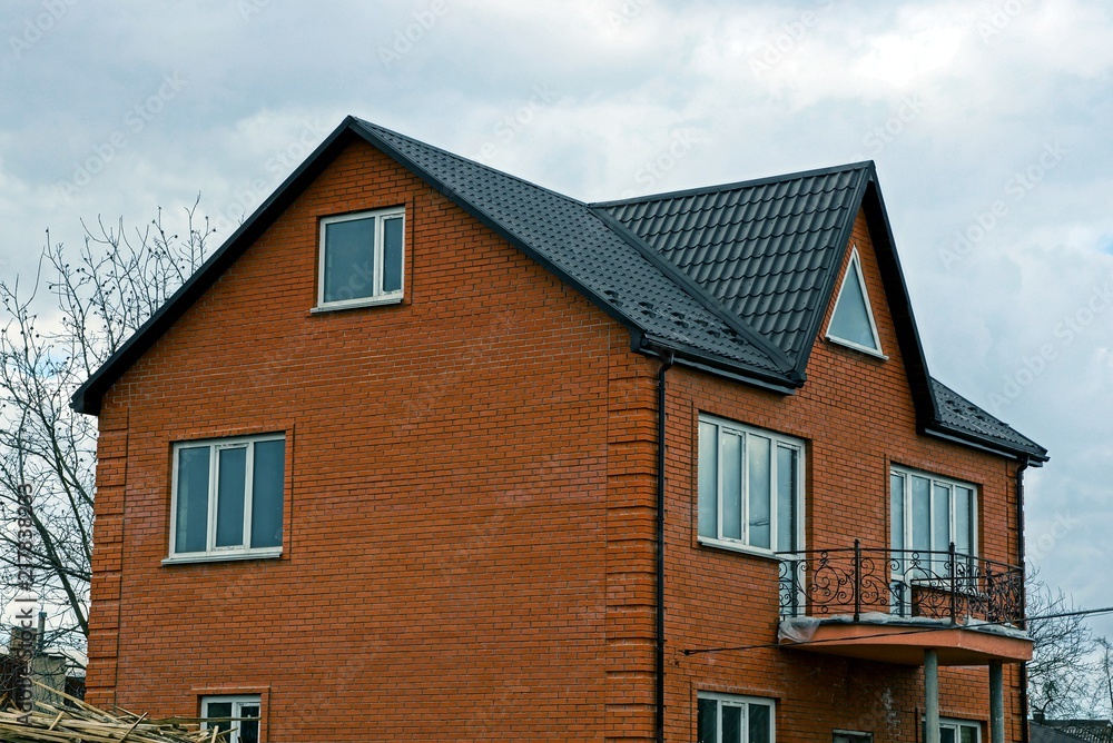 part of a large brick brown house with windows under a tiled roof