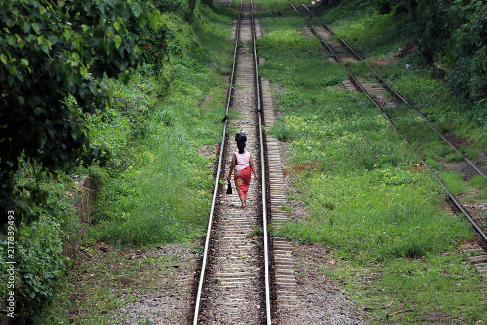 Fototapeta premium Behind of Myanmarese lady villager walking on the railroad tracks and put the black bag or belongings on the head.
