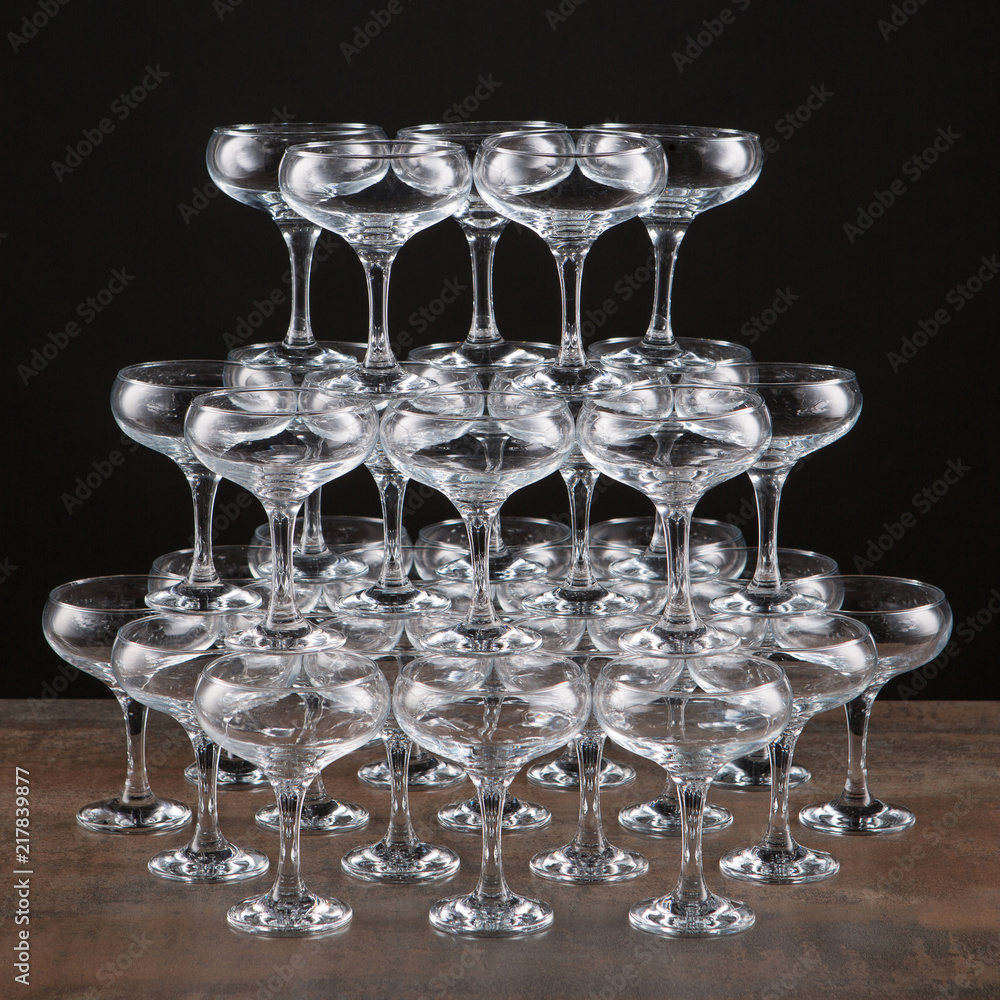 a lot of empty wine glasses on a brown table, built by a high pyramid, on a black background, isolate a lot of empty wine glasses on a brown table, built by a high pyramid, on a black background, isolate