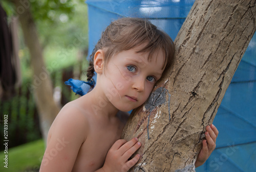 Portrait of a little four-years old girl, bending over a tree trunk. The child looks closely with her beautiful big blue eyes.