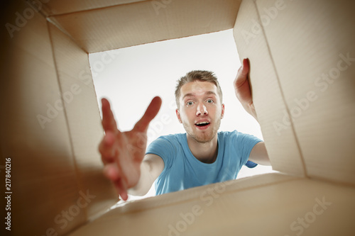Man smiling, opening box and looking inside. The package, delivery, surprise, gift and lifestyle concept