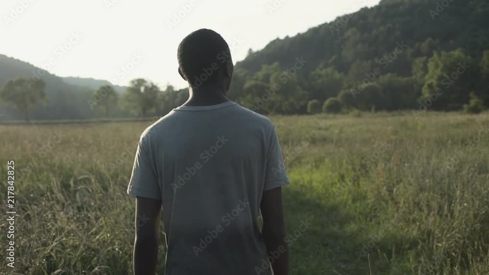 A young African boy walks alone through a field at sunset. A young African boy walks alone through a field at sunset.