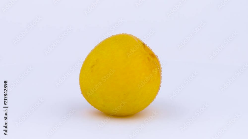 One whole big yellow plum on the turntable. Water drops appears on the skin during rotation. Isolated on the white background. Close-up. Macro. One whole big yellow plum on the turntable. Water drops appears on the skin during rotation. Isolated on the white background. Close-up. Macro.