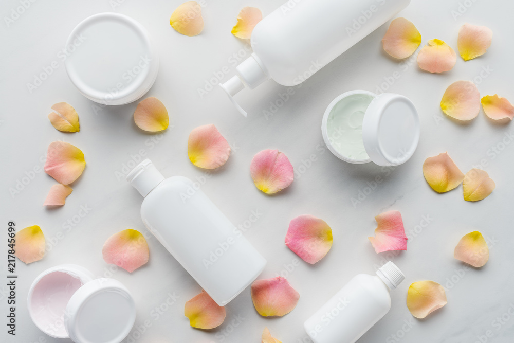 elevated view of bottles of cream and rose petals on white tabletop, beauty concept elevated view of bottles of cream and rose petals on white tabletop, beauty concept