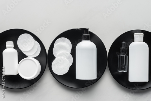 top view of bottles of cream and cosmetic pads on three black plates, beauty concept