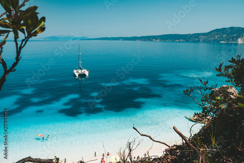 White catamaran yacht at anchor on clear azure water surface in calm blue lagoon. Unrecognizable tourists leisure on the beach