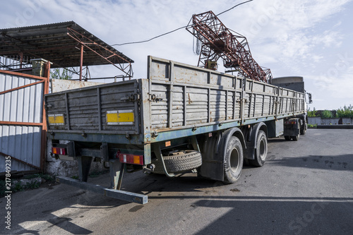 A truck with a gray trailer stands outside in daylight with a crane and a blue sky against a background. photo
