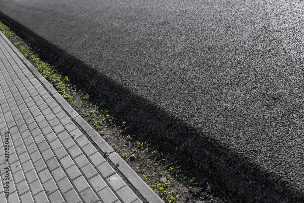 Obraz premium Close-up on a layer of new asphalt at the road under construction with a sidewalk road.