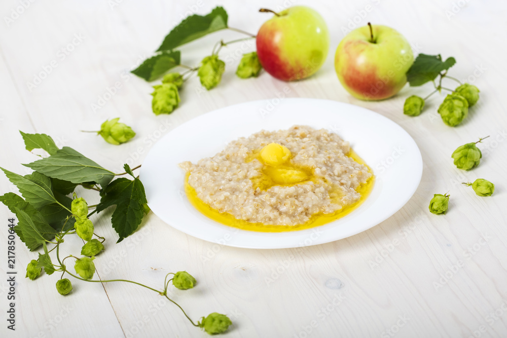 oatmeal porridge abundantly poured creamy melted butter on white plate among apples and hops and honey oatmeal porridge abundantly poured creamy melted butter on white plate among apples and hops and honey
