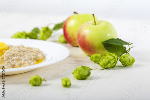 morning  oatmeal porridge abundantly poured creamy melted butter on a white plate among apples and hops. close-up