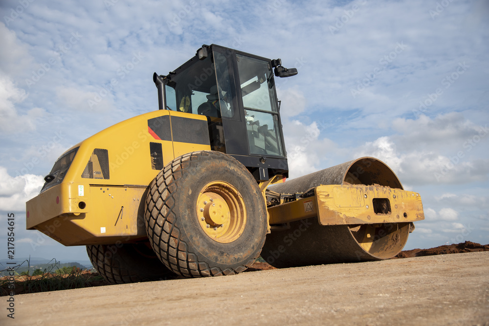 Yellow vibratory soil compactor working on highway construction site