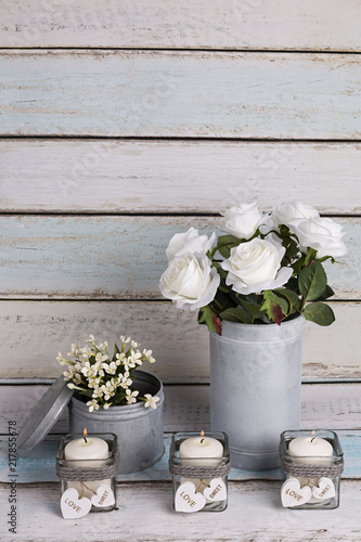 Florero vintage con rosas blancas y velas en portavelas de cristal.