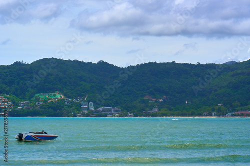 Motor boat sails in turquoise ocean water with green hills landscape of Phuket island in background.  Vacation destination. © Ruslan Kokarev