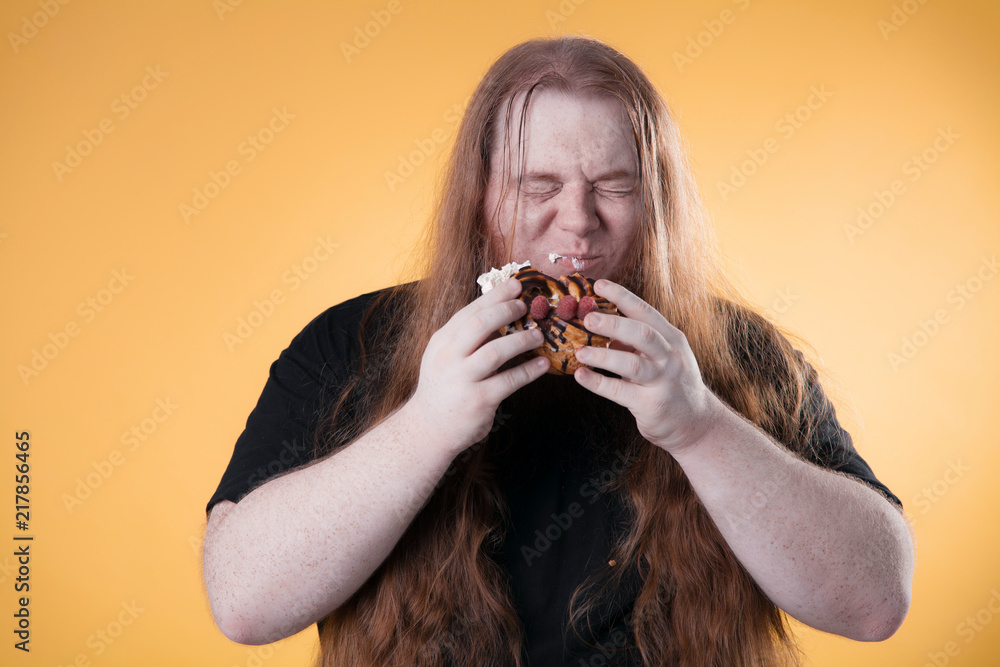 A fat man bites a big sweet cake. A hungry guy in the studio on a yellow background. A fat man bites a big sweet cake. A hungry guy in the studio on a yellow background.