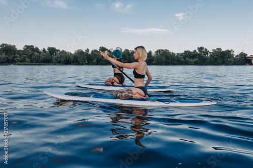 tattooed girls surfing on paddle boards on river