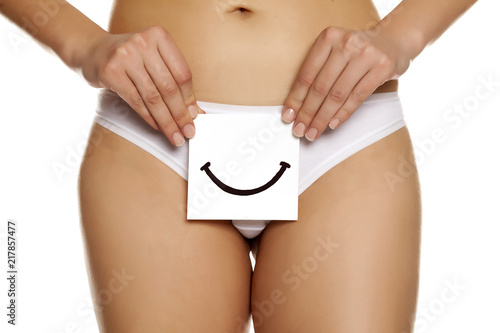 Woman in panties cowers her vagina with smile drawn on sheet of paper on white background