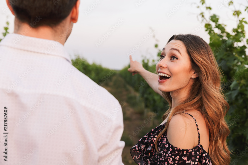 Fototapeta premium Joyful young couple man and woman smiling while walking outdoor together, through vineyard on summer day