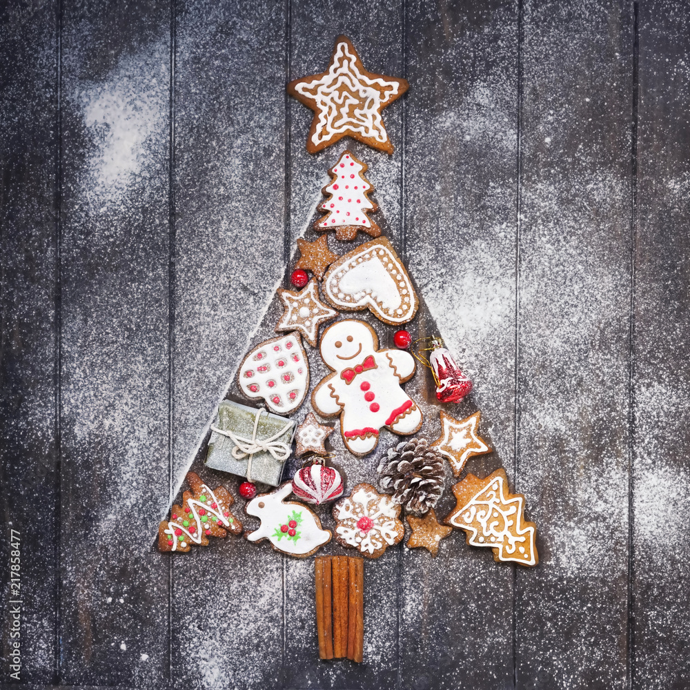 Christmas cookies in sugar icing, laid out in form of a Christmas tree on a brown wooden table, sprinkled with flour, flat lay. Christmas composition with gingerbread men, stars, fir-trees, rabbit.