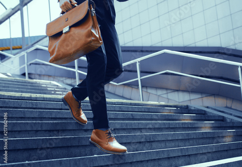 Businessman with bag in his hand walking down steps. Cropped shot of elegant man in suit taking step down on stairs. photo