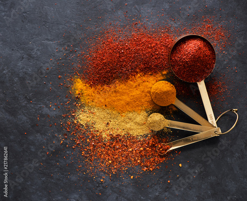 Fototapeta Naklejka Na Ścianę i Meble -  Powder spices and herbs in measuring spoons, on a black concrete background, top view