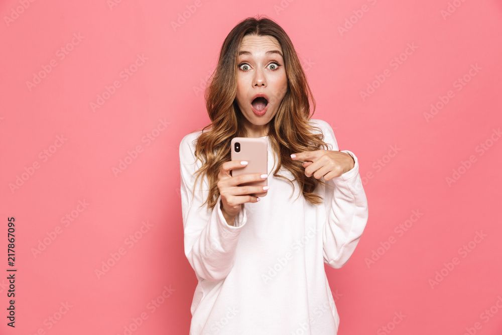 Image of excited caucasian woman with beautiful long hair screaming while holding cell phone in hand, isolated over pink background Image of excited caucasian woman with beautiful long hair screaming while holding cell phone in hand, isolated over pink background