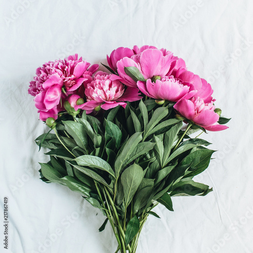 Flat lay  top view of pink peonies flower bouquet on white blanket background. Minimal summer floral concept.