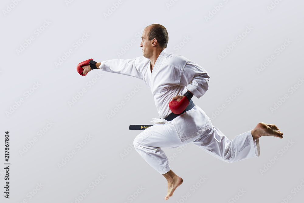 A man is training a punch with a hand in a jump against a light background
