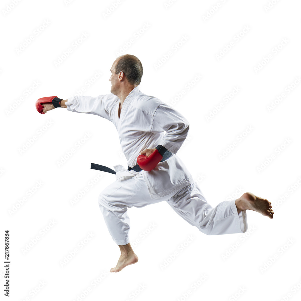 On a white background the sportsman with red overlays on hands trains a blow with his hand in a jump On a white background the sportsman with red overlays on hands trains a blow with his hand in a jump