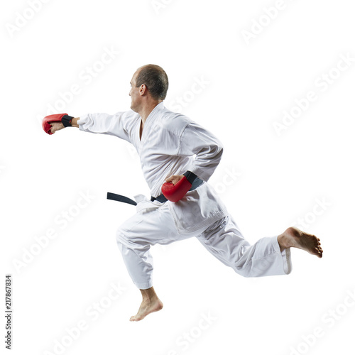 On a white background the sportsman with red overlays on hands trains a blow with his hand in a jump