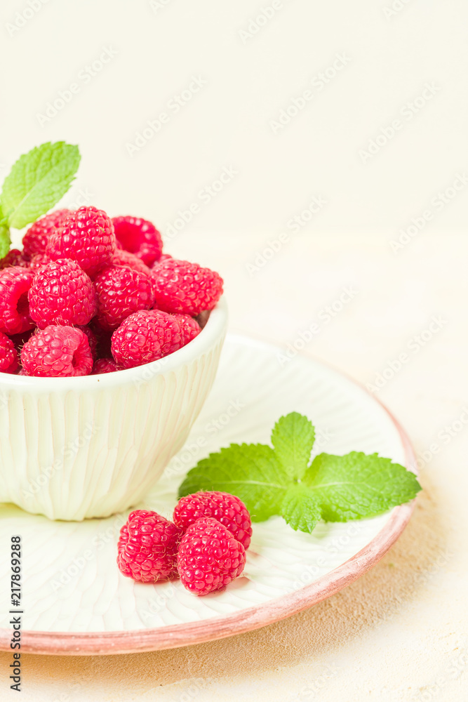 Ripe raspberries with green mint leaves in cup and saucer on pastel yellow background. Ripe raspberries with green mint leaves in cup and saucer on pastel yellow background.
