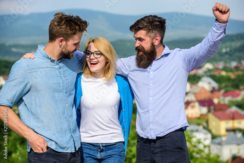 Company reached top. Business team concept. Men with beard in formal shirts and blonde in eyeglasses as successful team. Company of three happy colleagues or partners hugs outdoor, nature background