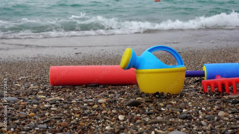 The concept of travel and vacation at sea, a family trip with children. Baby multicolored toys on the beach. Lake and rake for playing in the sand. The sea after sunset. The concept of travel and vacation at sea, a family trip with children. Baby multicolored toys on the beach. Lake and rake for playing in the sand. The sea after sunset.