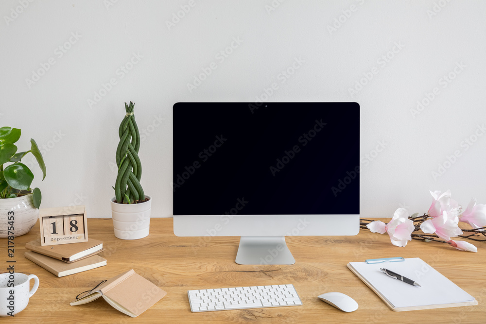 Naklejka premium Black desktop computer with mockup on desk with books and plants in work area interior. Real photo