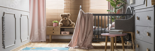 Panorama of a cozy, gray nursery bedroom interior with a classic wooden baby crib and pastel pink decorations photo