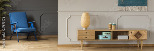 Schilderij op canvas Panorama of a vibrant blue armchair by a gray wall and a retro, wooden sideboard