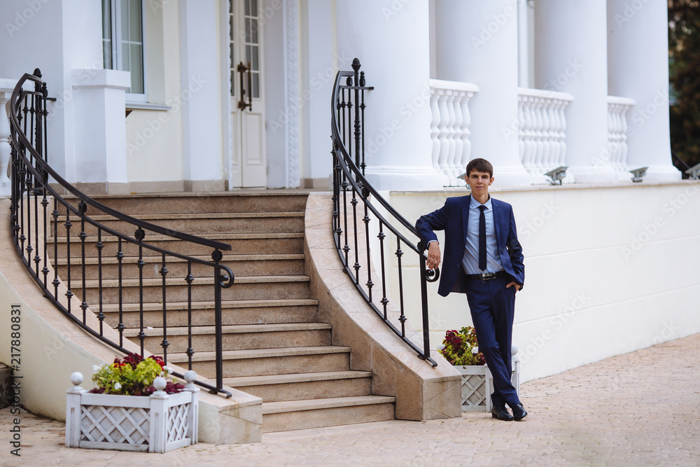 A man in a business dark suit is standing at the stairs on the street with his legs crossed and waiting for someone, he worries and smiles slightly. A man in a business dark suit is standing at the stairs on the street with his legs crossed and waiting for someone, he worries and smiles slightly.