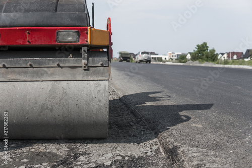 Orange Vibration roller compactor standing on a ground near asphalts road at road construction and repairing asphalt pavement works with a blue sky. photo